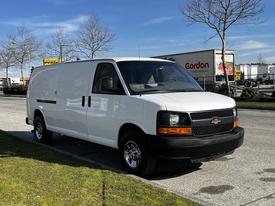 A white 2015 Chevrolet Express van parked on the side of the road with a simple design and chrome wheels