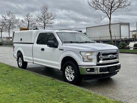 A 2017 Ford F-150 in white with a truck cap parked on a wet surface with its driver's side facing the viewer