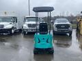 A turquoise 2024 AGT Industrial MH12R Mini Excavator with a tall black canopy positioned in front of several trucks in a parking lot