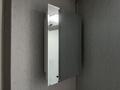 A mirrored medicine cabinet with a glass door partially opened revealing a textured inner panel