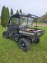 A 2015 John Deere 590m Gator in camouflage design featuring a roll cage large tires and a flatbed in the rear