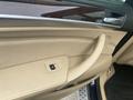 Close-up of the interior door panel of a 2009 BMW X5 featuring beige leather trim and a control button for the window