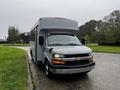 A gray 2015 Chevrolet Express bus parked with a large front cab and multiple windows on the side