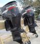 Two Suzuki outboard motor engines mounted on a wooden frame, featuring a sleek black design with red and white branding