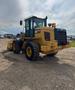 A 2016 CAT 938M wheel loader with large tires a yellow body and a front bucket attachment positioned in a gravel area