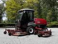 A red 2012 Toro Groundsmaster with a black cabin and multiple cutting decks positioned on a gravel surface