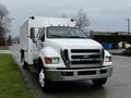 A 2013 Ford F-650 in front view with a white body and chrome grille featuring large front tires and orange clearance lights on the roof
