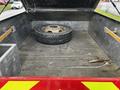 A 2007 Ford F-550 with an open truck bed containing a spare tire and some debris on the rubber mat lining the floor