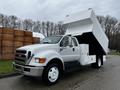 A 2013 Ford F-650 truck with a white box bed raised for dumping, featuring a silver front grille and large tires