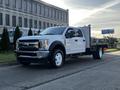 A 2018 Ford F-450 SD in white with a flatbed and toolboxes on the side parked on a road