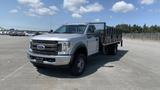 A 2019 Ford F-550 truck in silver with a flatbed and metal railing is parked in a large open area