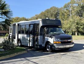 A 2019 Chevrolet Express shuttle bus with a black and white exterior parked with its doors open