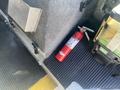 A red fire extinguisher is positioned on a black rubber floor mat next to a green and black container inside a vehicle