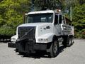 A white 2005 Volvo VND 122 truck with a dump bed sits prominently in the foreground featuring large headlights and a robust front grille