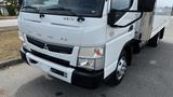 A white 2018 Mitsubishi Fuso FE160 truck with a flatbed and visible branding on the front bumper