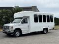 White 2014 Ford E-350 shuttle bus with large windows and a boxy design parked on a lot