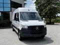 A 2019 Mercedes-Benz Sprinter van in white with a black front grille and tinted windows parked in a lot