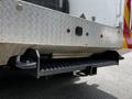 Close-up of the rear of a 2009 Ford F-550 showing a black hitch receiver and textured step mounted beneath a metallic checker plate bumper