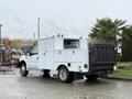 A white 2000 Ford F-450 utility truck with a service body and a black bed is parked at an industrial site