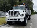 A 2017 International WorkStar 7600 truck with a white body and chrome grille featuring an elevated cab and a flatbed with a loading mechanism on the back