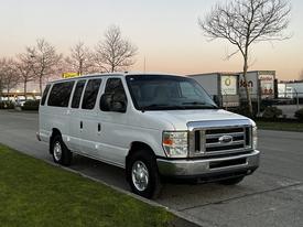 A white 2012 Ford Econoline van with a chrome front grille and large windows parked on a driveway