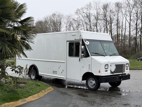 A white 2012 Ford Econoline delivery van with a boxy design and a blank side panel parked on a wet surface