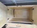 A 2013 Ford Econoline open cargo area with wooden cabinets featuring metal hinges and a pull handle in the foreground