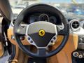 Black leather steering wheel with a yellow Ferrari logo at the center and control buttons on either side located in the interior of a 2005 Ferrari 612 Scaglietti