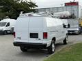 A white 2013 Ford Econoline van with a ladder rack on top parked at a location with other vehicles nearby