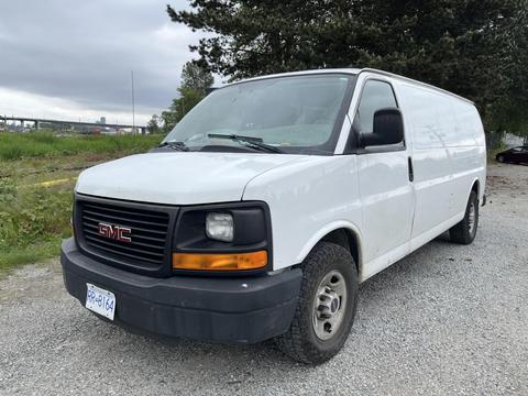 2014 GMC Savana van with a white exterior and black front grille parked on gravel with no visible load or cargo inside