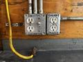 A close-up of electrical outlets with labels for inverter and generator, connected by a yellow extension cord, mounted on a metal surface