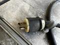Close-up of a power cord plug with prongs and a black and white plastic housing resting on a metallic surface