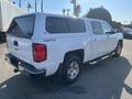 A white 2015 Chevrolet Silverado 1500 pickup truck with a camper shell on the bed displaying the 4x4 badge and chrome side steps
