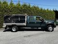 A green 2008 Ford F-550 with a flatbed and black storage boxes on the side parked on a gravel surface