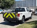A white 2016 Ford F-150 pickup truck with a black and yellow striped tailgate and 4x4 emblem parked with other vehicles in the background