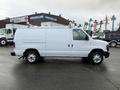 A white 2013 Ford Econoline van is parked with its side profile visible showcasing its sliding door and roof rack