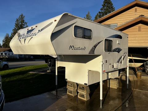 A 2023 Westland 80W 8 Foot truck camper with a modern design and a white exterior perched on supports in a residential driveway