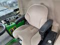 A plush beige seat with armrests designed for a John Deere 1585 Terrain Cut featuring controls and a green base