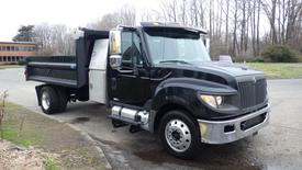 A black 2012 International TerraStar dump truck with a flatbed and toolbox on the side parked on a lot