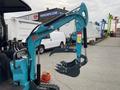 A blue 2024 AGT Mini Excavator with a claw attachment for gripping materials is positioned prominently in the foreground