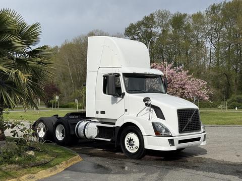 A white 2012 Volvo VNL truck with a sleek design parked with a tall cabin and distinctive grille showcasing its robust build and modern features