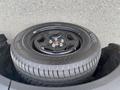 A black wheel with a tire mounted on it resting on a vehicle's storage compartment