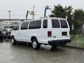 A white 2013 Ford E-350 van parked with its rear facing the viewer showing its large sliding side door and high roof design