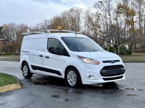 A 2017 Ford Transit Connect van with a white exterior and roof racks positioned at an angle on a wet surface