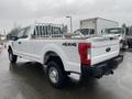 A white 2017 Ford F-250 Super Duty truck with a metal rack in the bed and off-road tires parked on a wet surface