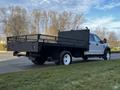 A 2018 Ford F-450 SD with a flatbed design featuring a black metal railing and dual exhaust pipes parked on a grassy area