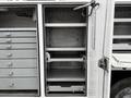 A 2017 Ford F-550 service truck with open side storage compartments featuring several shelves and drawers designed for tools and equipment storage