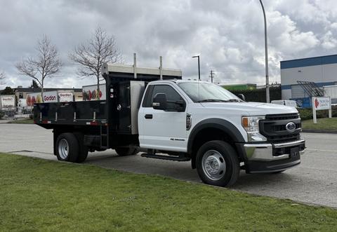 A 2021 Ford F600 truck with a flatbed and tool storage on the back parked on grass