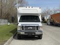 A 2010 Ford Econoline with a white shuttle bus body and large front bumper positioned straight on in the foreground