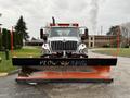 A 2012 International 7400 equipped with a large orange and black snow plow attachment in the foreground